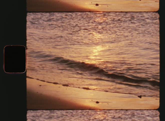 Ms Super-8 footage of light ocean waves washing up on the sand beach at sunset with warm tones and the rippling water moves making the reflection of the sun bounce back and forth