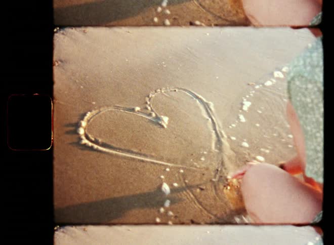 A woman in love drawing a heart in the sand before it gets washed away by the sea waves while enjoying the lovely evening by the beach on a warm summer day with coastal vibes and vintage flair