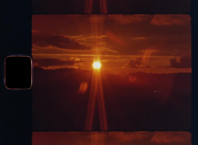 8mm film footage of a sunset at the horizon while the sun shines through clouds and causes a bright lens flare