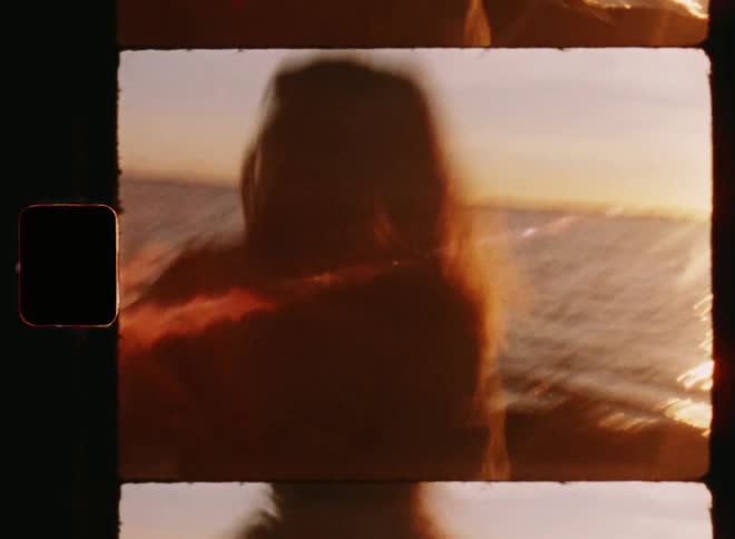 Young brunette woman in love smiles in a happy way as she grabs the hand of her boyfriend and they run towards the sea during the sunset on a sandy beach on a summer vacation on vintage 8mm film