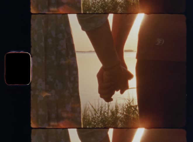 8mm film footage of a young man and woman standing next to each other grabbing and holding each other’s hands looking out over the water while dating on a warm summer evening by a countryside lake