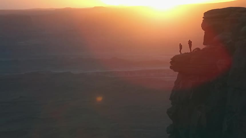 Two people stand on a ledge at sunset