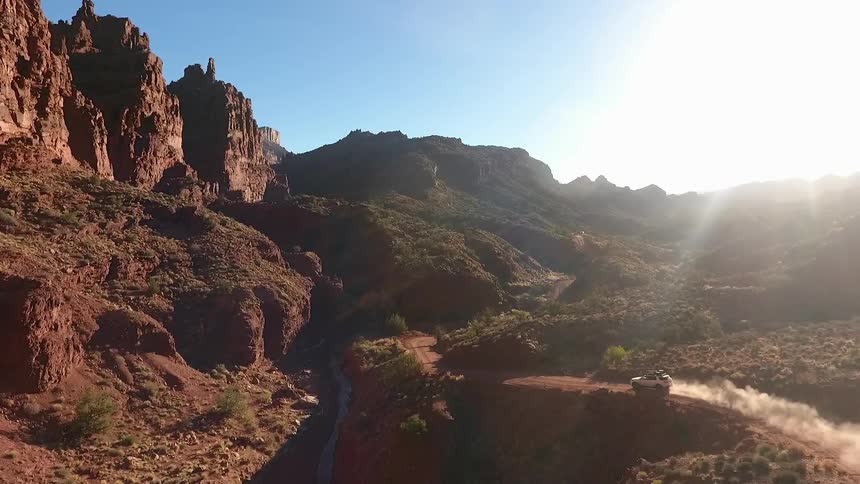 A vehicle is traveling along a dirt road near a canyon