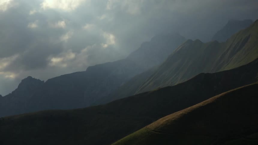 Sunlight shining through heavy clouds on grassy mountains