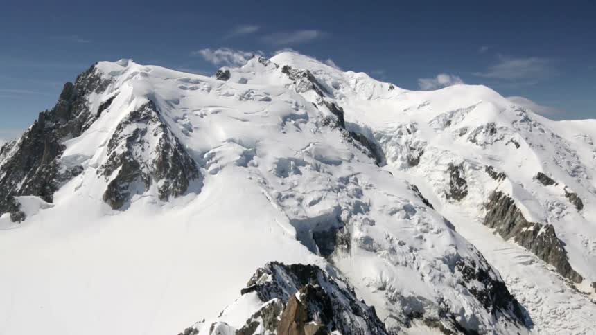 Wispy clouds hover above snow-covered mountain tops