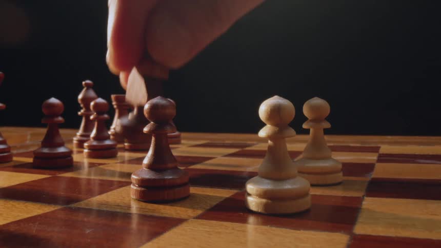 A man moves a chess piece on a wooden board