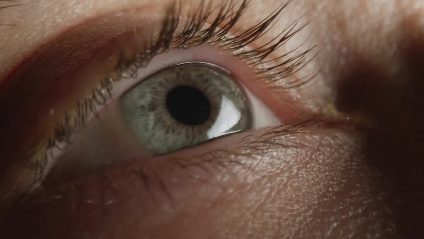 A very close up view of a person opening their hazel colored eye and the pupil moving