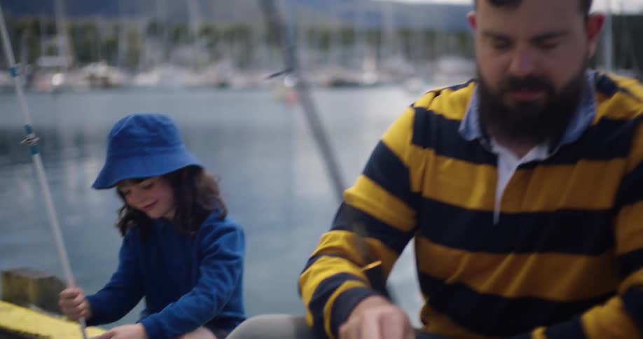 A man speaks with a little girl as they fish together on a pier during the day