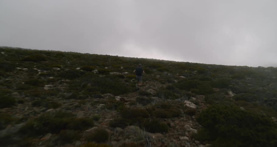 Man with cap black t shirt and shorts jogs in barren field on cloudy day