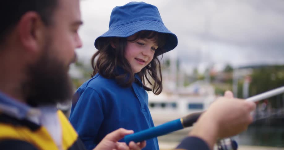 A father fishing with his daughter hands her a fishing pole
