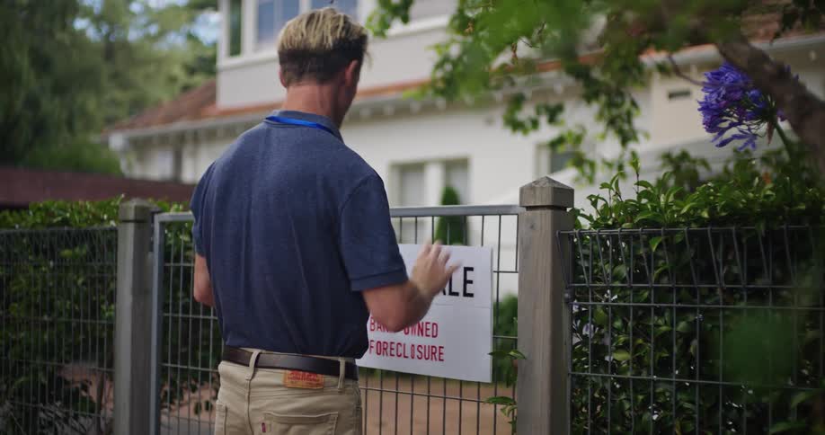 A man hangs a for sale sign outside a foreclosed home