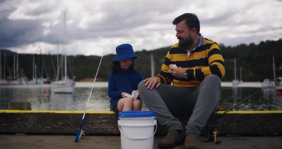 A man and his daughter take a break from fishing to eat sandwiches