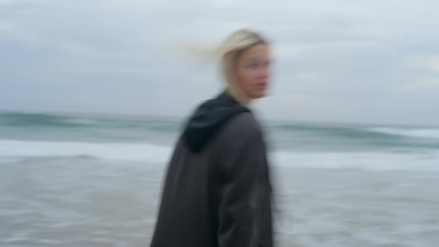 Blonde woman with gray jacket walks into ocean on cloudy day
