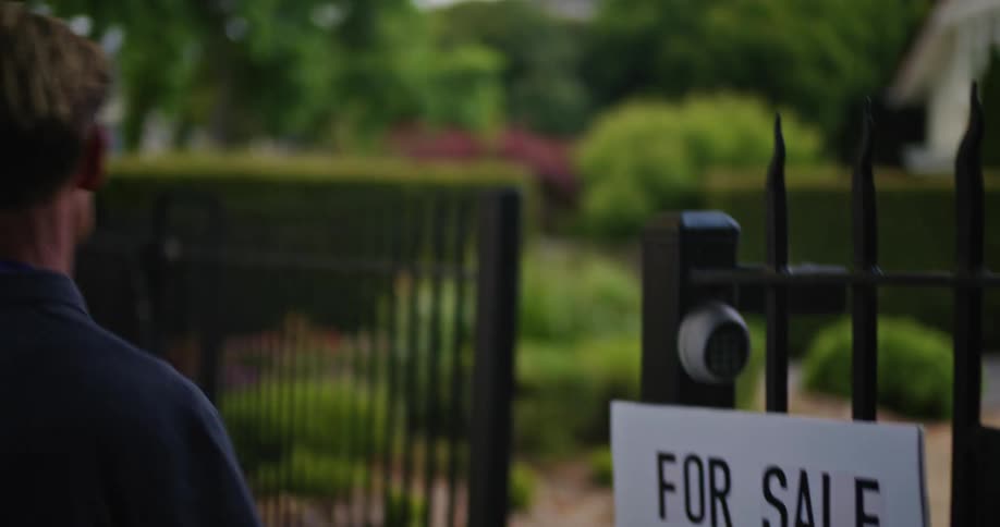 A man hangs a foreclosure sign on a fence outside a home