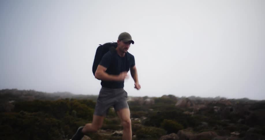 A man wearing a backpack runs over rocky terrain in the wilderness on a foggy day