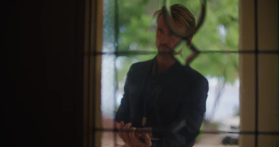 A man stands outside a home and writes on a clipboard as he looks around