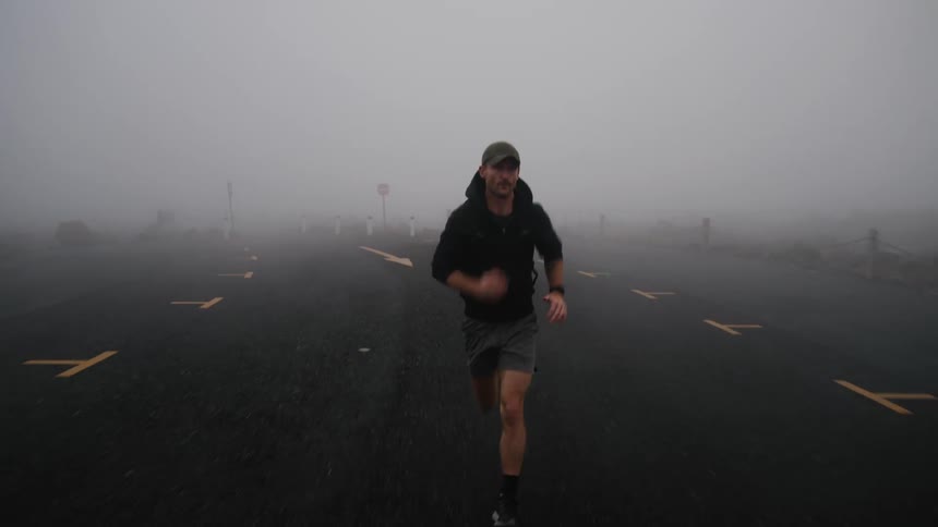 A man wearing a backpack runs along a road on a foggy day