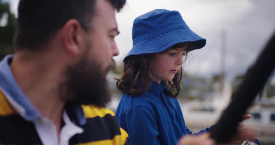 A man and his young daughter are on the dock with fishing poles as he is teaching her how to fish