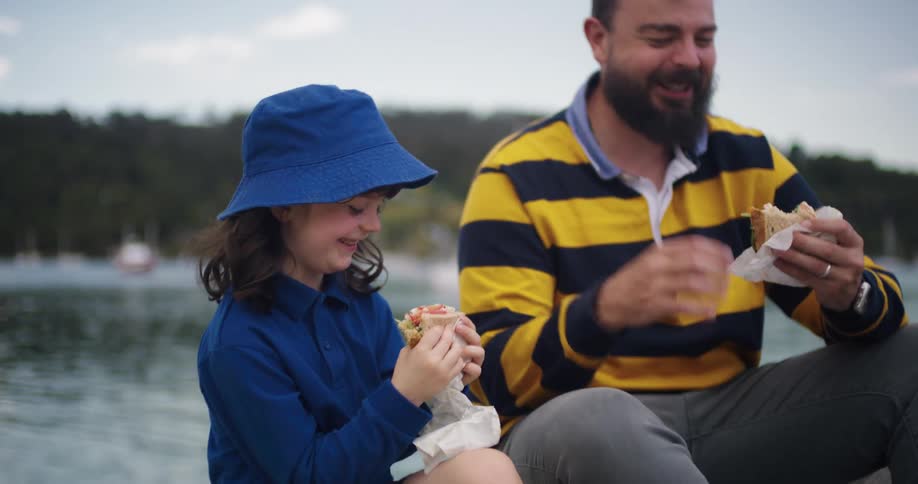 A man and his daughter eat sandwiches while sitting on a boat in a lake