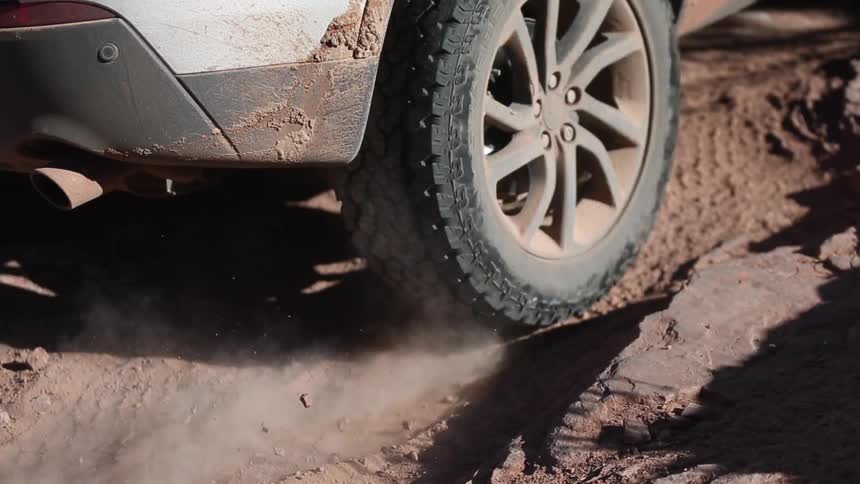 A vehicle's rear tire struggles to gain traction on a dirt road