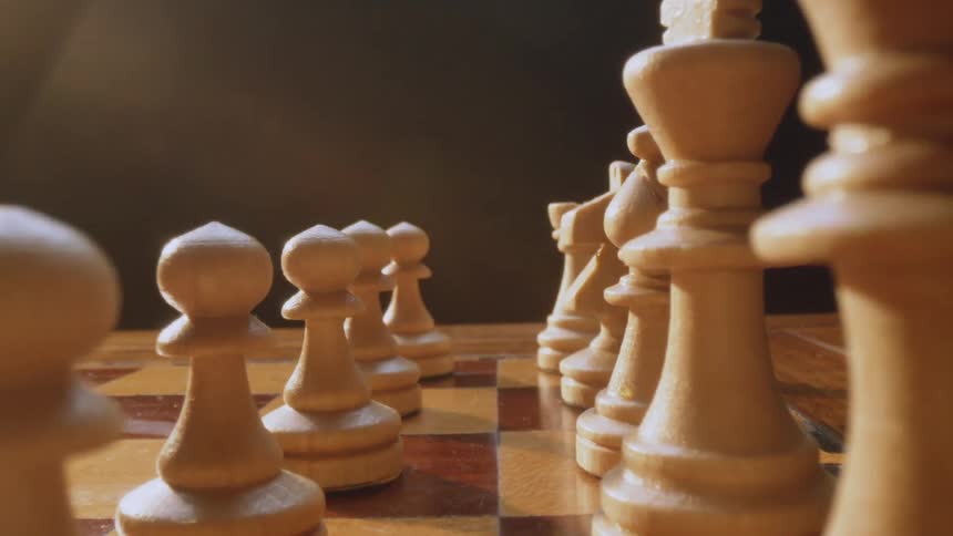 Wooden chess pieces are lined up on a board