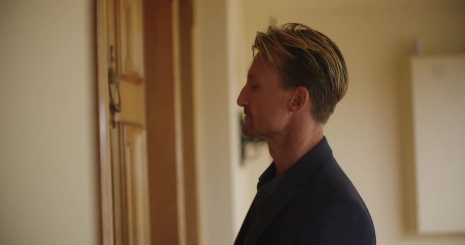 A man knocks on a door while looking around at his surroundings