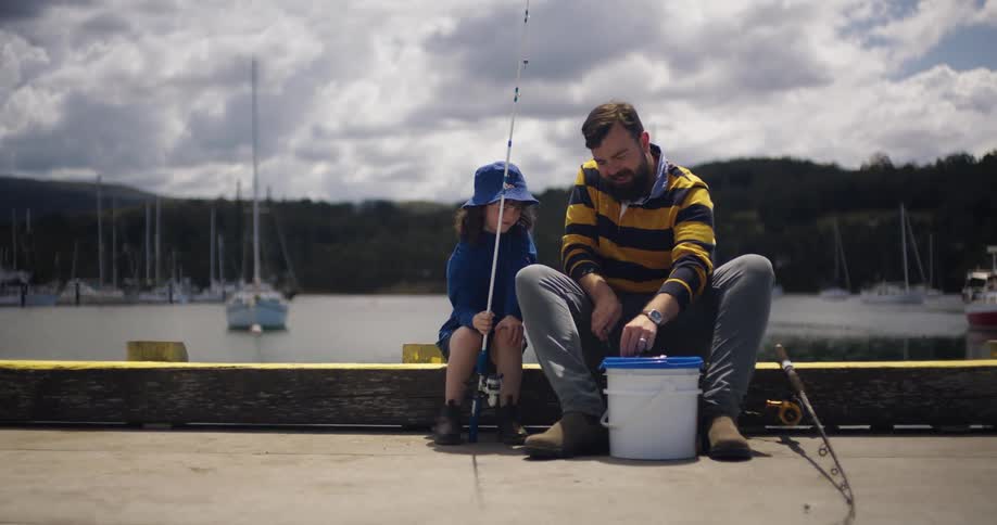 A man shows his daughter how to attach bait to a fishing line