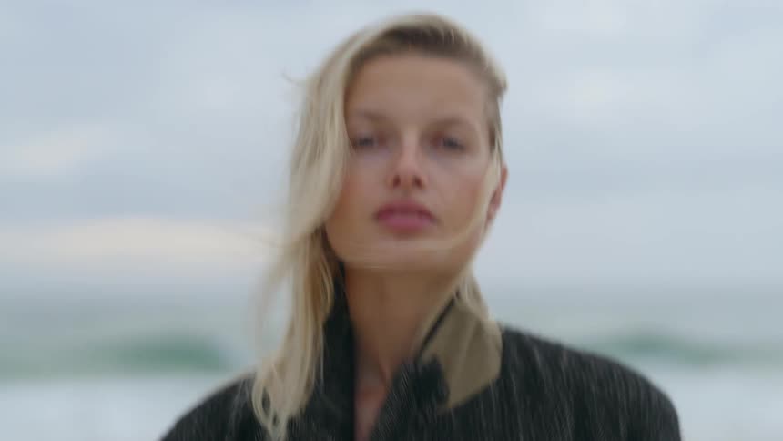 Wind blows through a womans hair while she stands on the beach