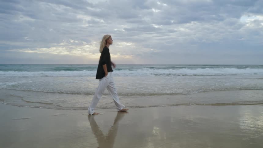 A woman is walking on the coast of a beach