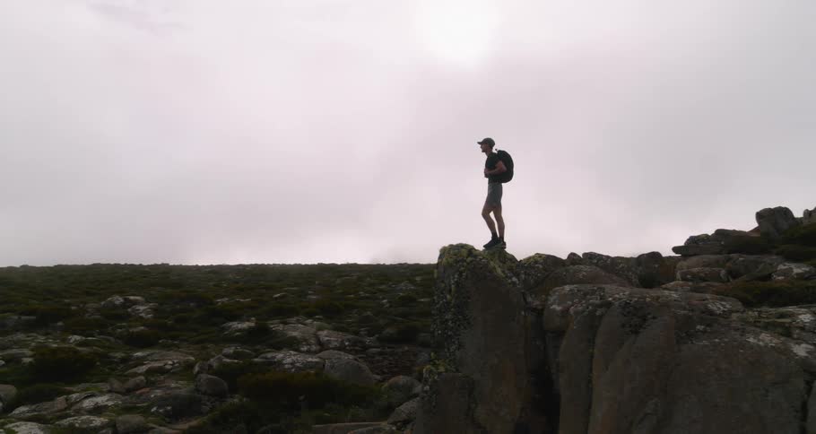 Hiker stands on boulders looking over rugged valley under an overcast sky