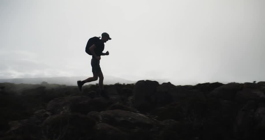 A man jogging with a large backpack over rocky terrain in nature