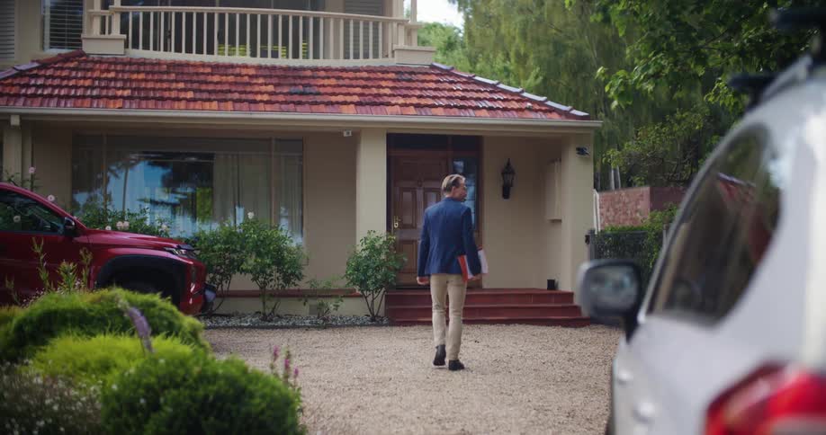 Man in dark blue blazer and brown pants walks and enters house in the countryside