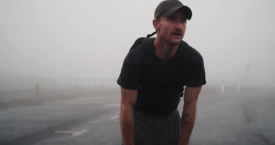 Man with cap black t shirt and shorts jogs on highway in fog