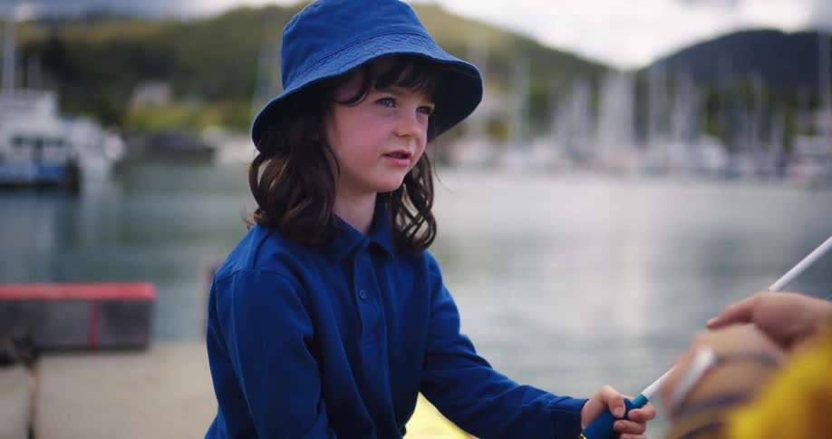 Daughter hands her fishing pole to father as they fish across from marina