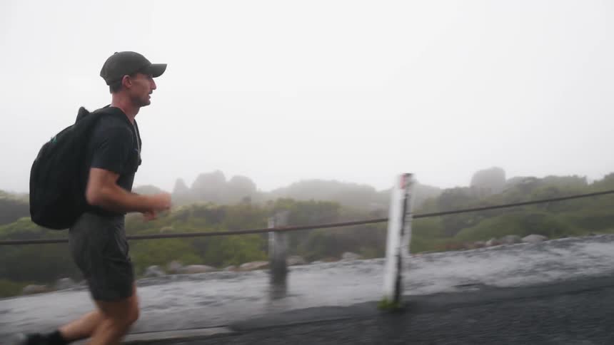 Man carrying backpack jogs along road near sidewalk on foggy day