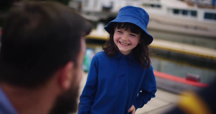 A little girl is standing on the dock smiling as she talks to her father