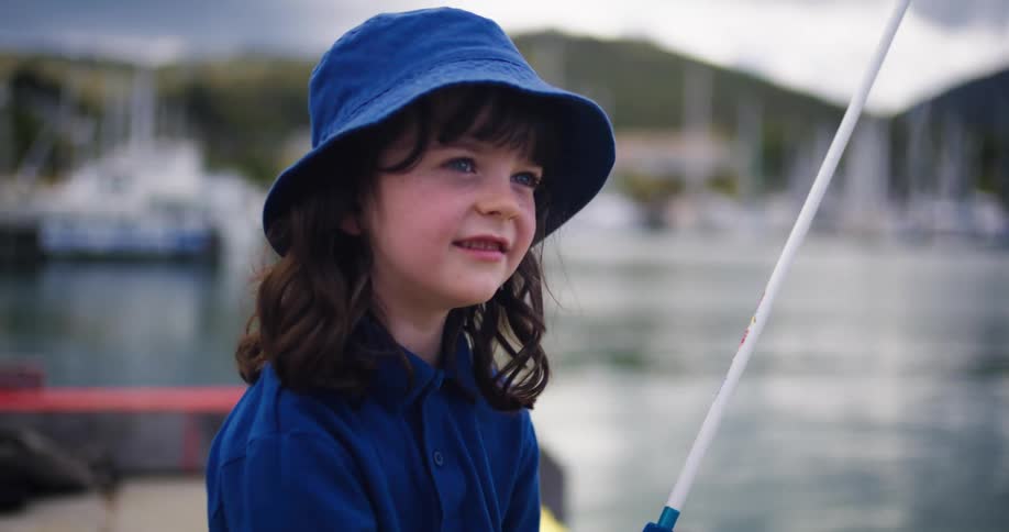Girl wearing bucket hat sits on boat near marina fishing
