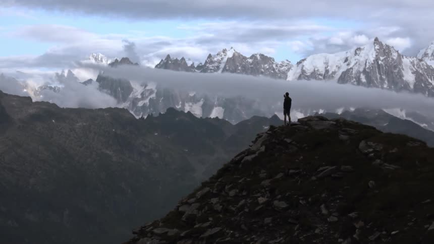 A man stands atop a hill and looks out on a vast mountain range