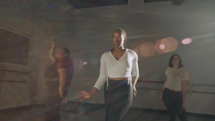 Four women moving their arms and dancing slowly in a room with sunshine shining in