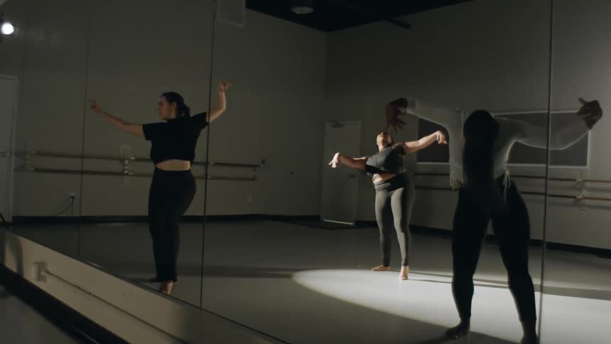 Three women dancing in front of a mirror with a spotlight in the middle of the room