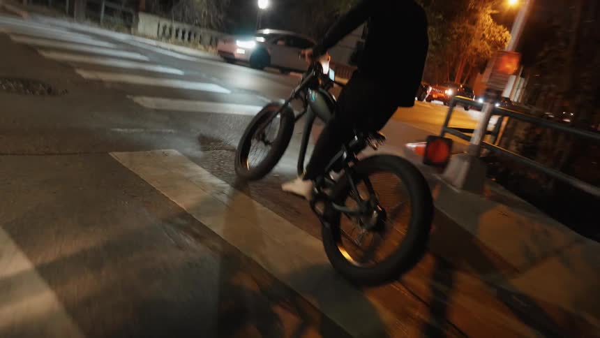 A man standing on a motorbike while riding it down the street and around a corner