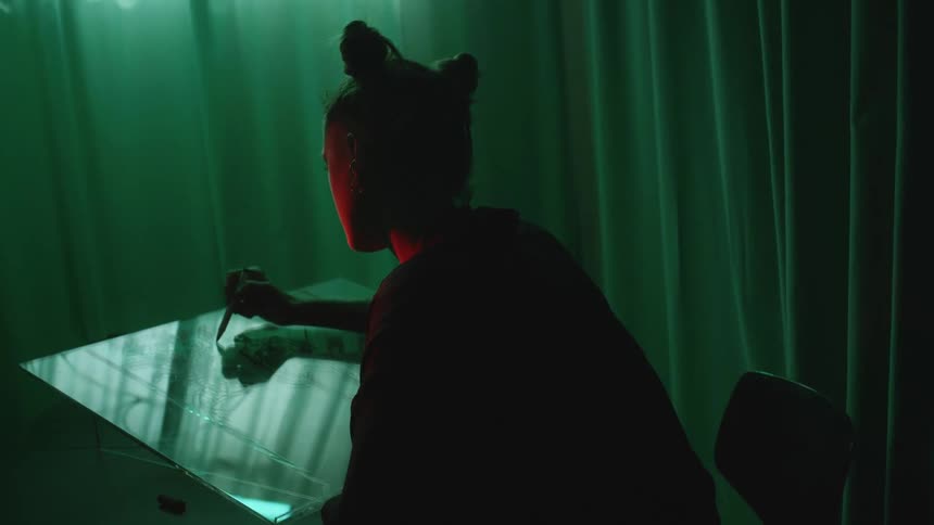 A female is sitting down and sketching indoors