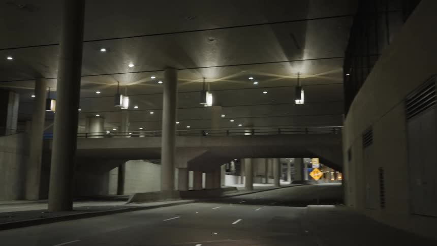 Lights glow over a road leading through a tunnel as a person moves across the bridge above