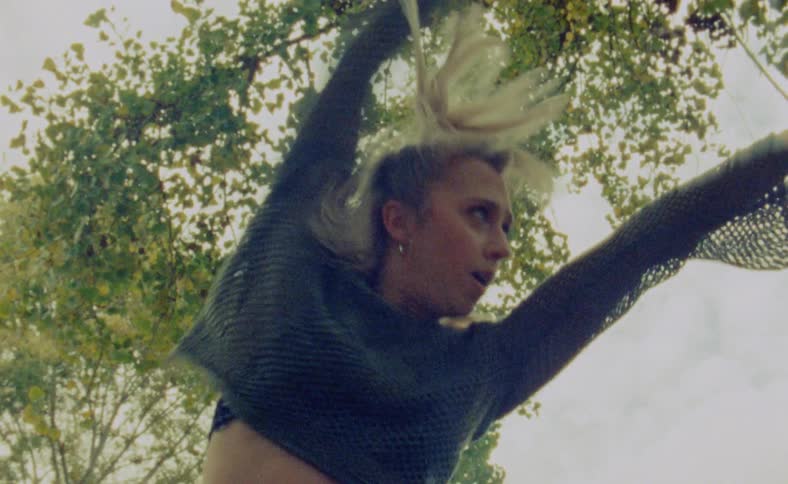 A young woman is dancing outside in the middle of the day time