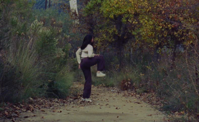 A woman is dancing outside on a path in between trees