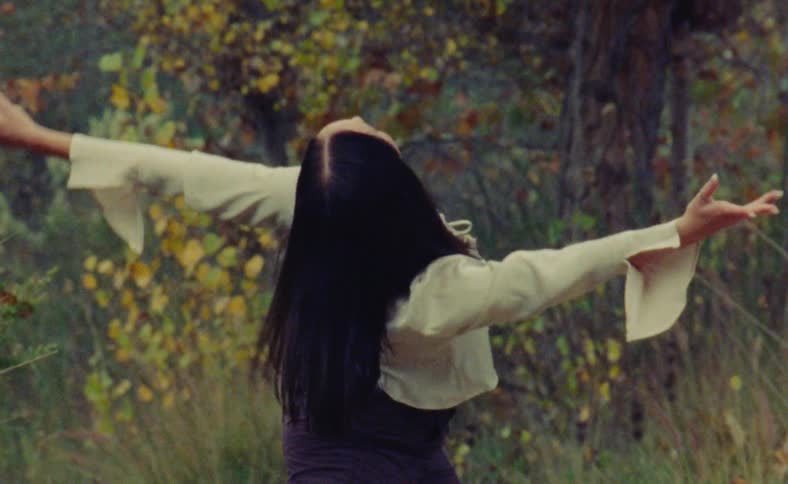 A woman is doing interpretive dance movements outside in nature