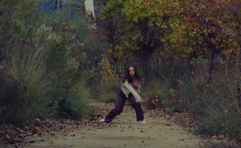 A woman is doing interpretive dance movements outdoors on a path surrounded by trees