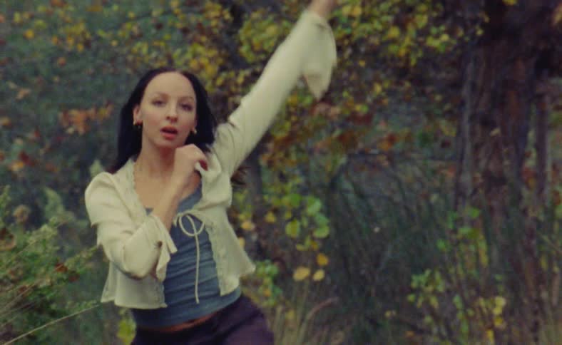 A woman is dancing outdoors in a forest area