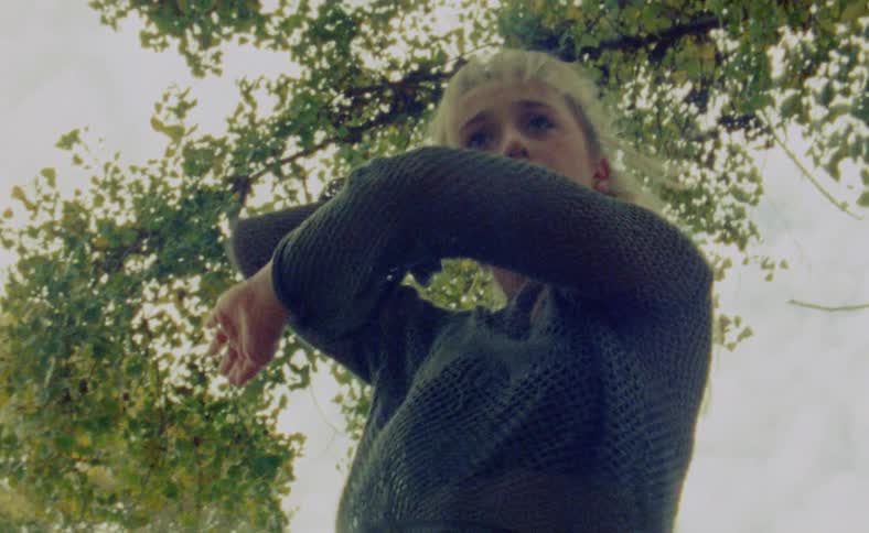 A woman is dancing outdoors in a wooded area