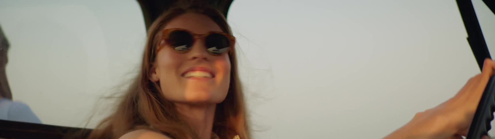 Smiling woman wearing sunglasses drives a car on a sunny day